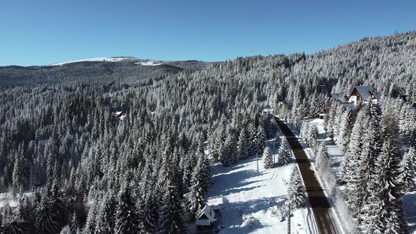 Aerial Shot with Road in a Forest Covered in Snow on a Sunny Winter Day, Drone Video Winter Mountain