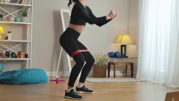 Young Slim Woman Doing Squats with Resistance Band on Legs. Concentrated Confident Beautiful