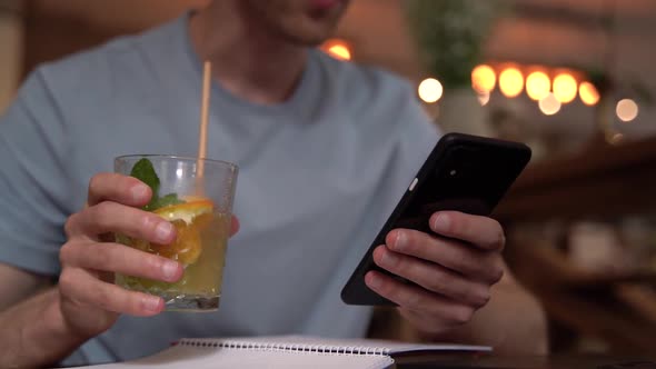 Close-up view. In the hands of a man a smartphone and a glass of refreshing lemonade