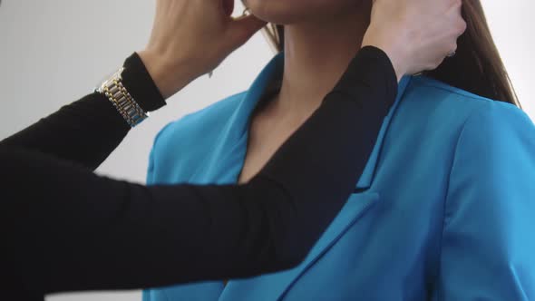 Designer Adjusts the Jewelry Around the Neck of a Beautiful Woman in a Blue Blazer