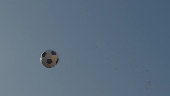 Slow motion wide shot of a soccer ball (football) flying through the air. Grass trails behind the ba