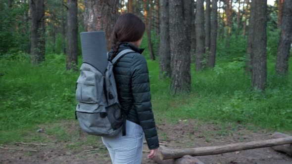 Young Woman in Camping Clothes and with a Backpack Stops in the Forest