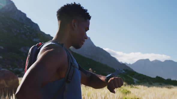 African american man cross country running in mountain countryside using smartwatch