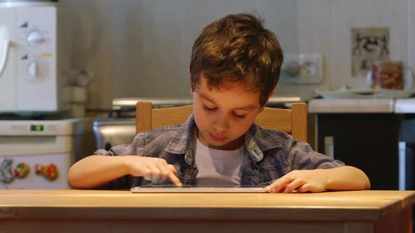 Cute Little Child Uses A Tablet Pc At A Table At Home