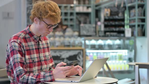 Young Redhead Man Working on Smartphone and Laptop