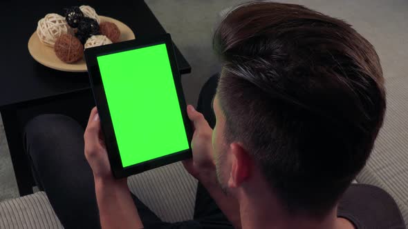 A Man Watches a Tablet with a Green Screen Vertically in Living Room