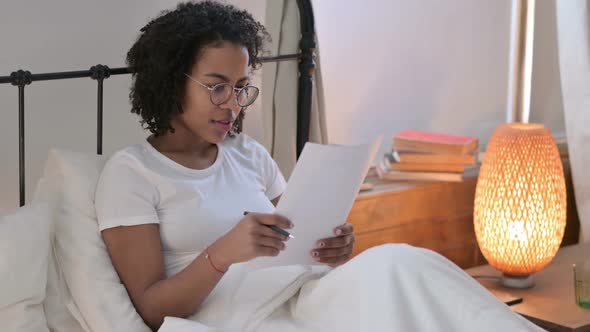 African Woman Reading Documents in Bed