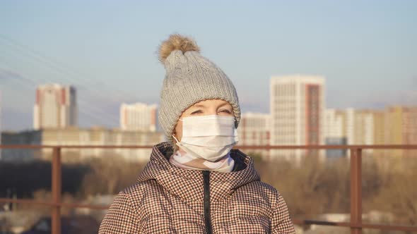 Portrait of a Girl in a Medical Mask, Warm Jacket and Hat on the Street Looking at the Camera