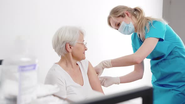 Young Attractive Blonde Nurse Vaccinating the Senior Gray Haired Lady in Hospital Room Immunization