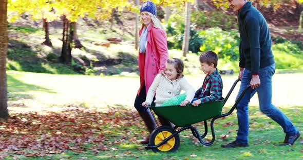 Parents carrying their son and daughter in a wheelbarrow