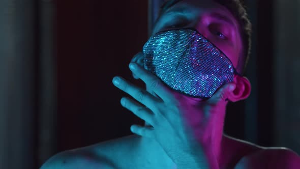 A Young Flirty Man Stripper Acting Sexy in Neon Lighting Wearing Mask with Rhinestones