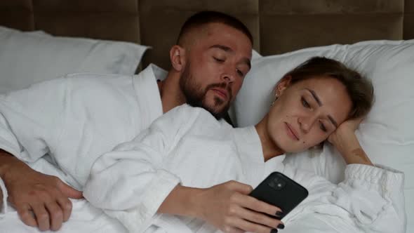 Man and Woman in Bed in Morning Lady is Viewing Social Nets in Smartphone