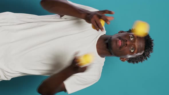 Playful Adult Juggling Lemons and Standing Over Blue Background