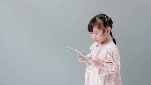 Child watching cartoon with digital tablet in studio with gray background. Capture with Copy Space.