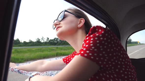 Young Girl with Scarf in Her Hands Leaning Out of Window of Vintage Car