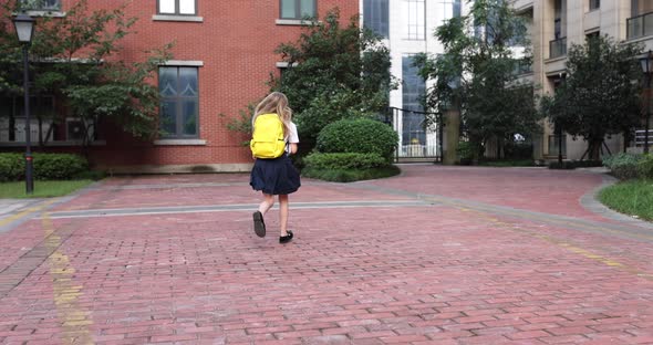 Happy Little Caucasian Blonde Girl Seven Years Old in Uniform with Yellow Backpack Running Back to