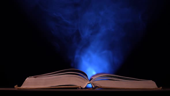 In a Dark Smoky Studio a Thick Open Book Lies on a Table Against a Black Background