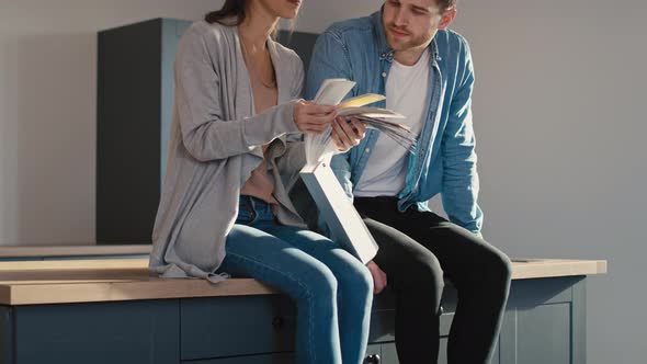 Tilt up video of caucasian young couple sitting on kitchen island and picking colors for walls.