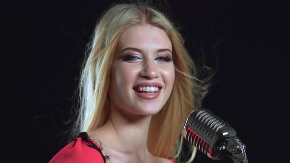 Girl in a Red Dress Is Singing Into a Retro Microphone. Black Background. Close Up