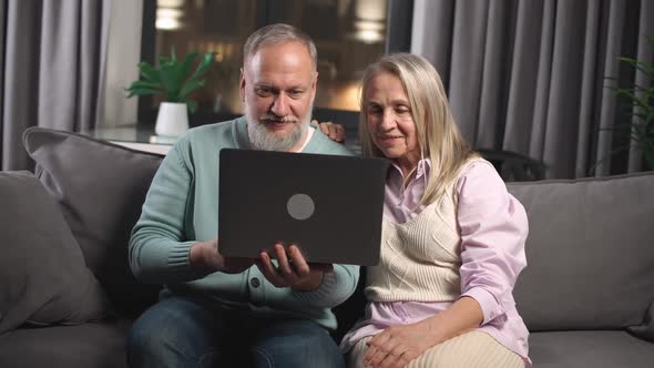 An Elderly Couple Sits on a Sofa in the Living Room an Adult Man and Woman Use a Laptop and