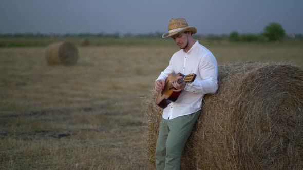 Man Wearing a Straw Hat Playing the Guitar About a Haystack