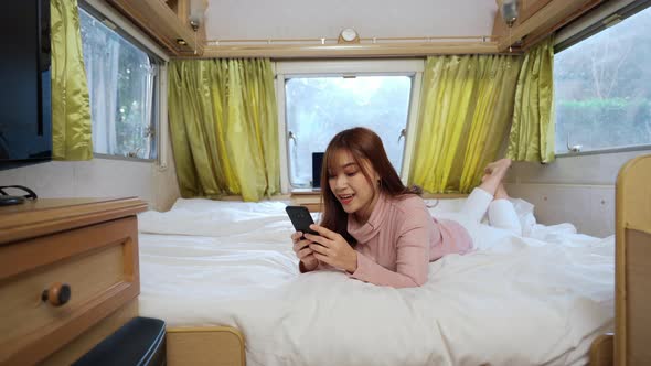 young woman using smartphone on bed of a camper RV van motorhome