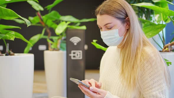 Woman in a Protective Mask Next to the Wifi Icon is Watching in a Smartphone