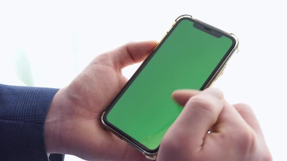 Man Using Smart Phone in Office Space Sitting on Chair and Using Green Screen Phone Mockup Chroma