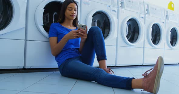 Woman using mobile phone at laundromat 4k