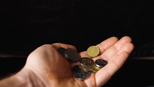 Various coins fall into a man's palm against a black background. Slow motion. Close-up