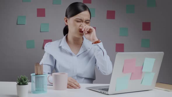 Asian woman working on a laptop sitting at home office was sick with stuffy nose breathless.