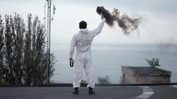 Man in Protection Suit Standing on the Edge of the Roof with Smoke Stick
