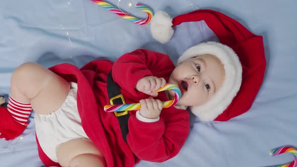 Smiling Funny Newborn Baby in Santa Claus Hat Red Bodysuit Play on White Soft Bed Lick Sweet