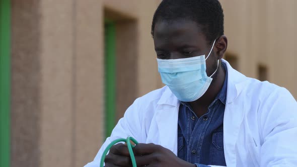 pandemic - worried black doctor sitting on the stairs wearing the mask shakes his head