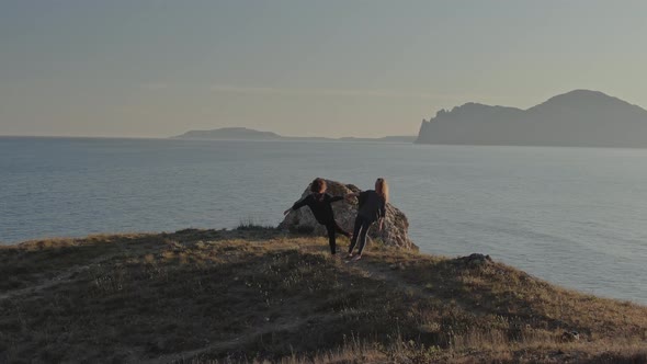 Two Women in Sportswear and Barefoot Doing Yoga Exercises and Laughing on the Seashore Against the