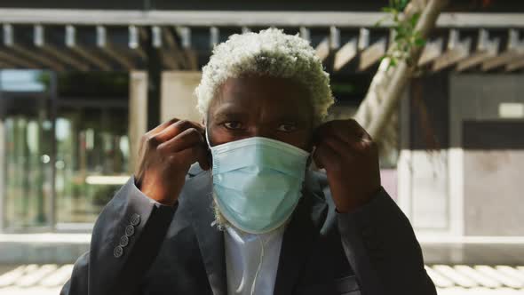 Portrait of african american senior man in facemask wearing earphones in corporate park