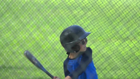 A boy hits a ball in a batting cage at little league baseball practice.