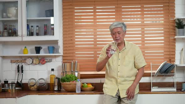 Portrait senior Asian man drinking water in the kitchen at home.