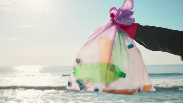 A volunteer in protective gloves holds a plastic bottle and puts it in a garbage bag