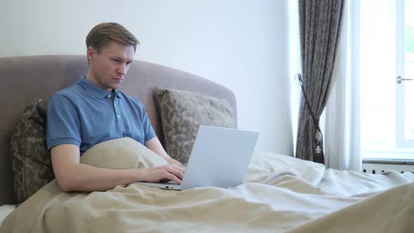 Adult Man Working On Laptop while Sitting  in Bed