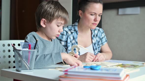 The camera moves to a boy making a wooden toy with his mom