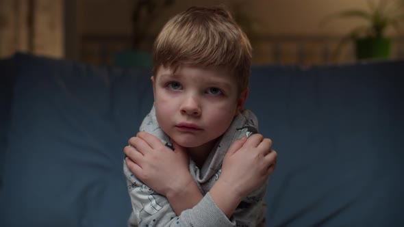 Portrait of Young Upset Boy Sitting on Couch at Home. Sad Kid's Face Looking at Camera in Slow