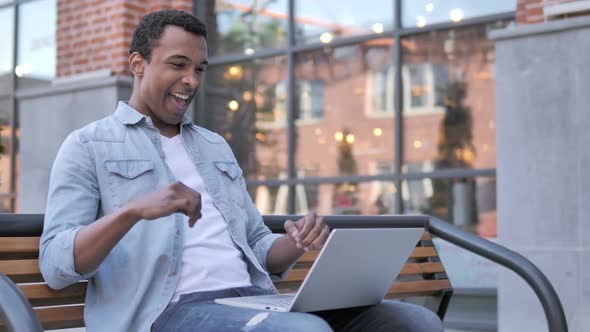 African Man Celebrating on Laptop Sitting Outside Office
