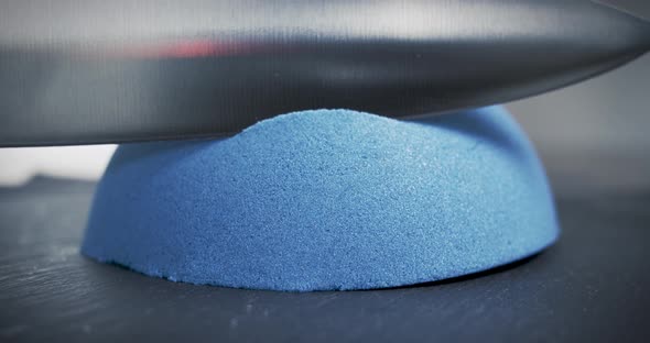 Hemisphere of blue kinetic sand is cut with a large knife. Relaxation techniques. Close-up.