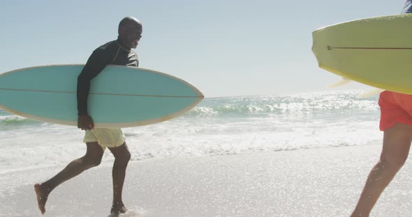 Smiling senior african american couple running with surfboards on sunny beach