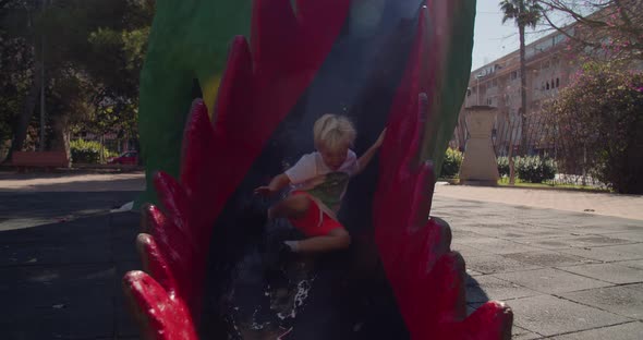 Happy Child Comes Down the High Dragon Children's Slide and Runs on Summer Day