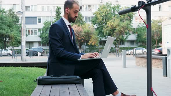 Man in Business Suit Typing on the Laptop Outdoor of His Office in the City