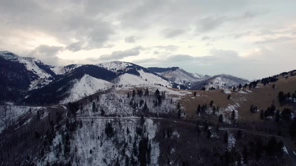 Stormy drone shot over a mountain range with a winding road and snow peaks