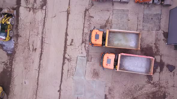 Aerial shot of bulldozer and trucks in outside warehouse. Drone