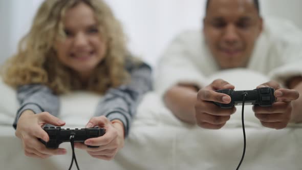 Closeup Male and Female Hands Pressing Keys on Gamepad with Blurred Interracial Couple Lying on Bed